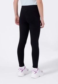 Leggings negros confeccionados en tela elástica, con una cintura alta. Combinados con zapatillas blancas acentuadas con detalles morados.