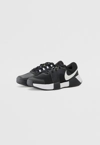 Crne atletske tenisice od mrežaste i gumene tkanine. Imaju zaobljeni vrh, bijeli swoosh logo, zelene akcentne boje i teksturiran potplat.