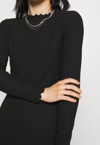 Černé žebrované šaty s dlouhými rukávy, se scalloped výstřihem a manžetami. Textura je hladká s přiléhavým siluetou.