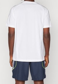 Camiseta blanca de manga corta con cuello redondo; combinada con pantalones cortos azul marino con detalles en verde neón y bolsillos laterales.