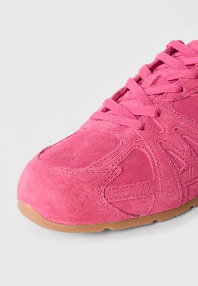 Różowy zamszowy sneaker z teksturowanymi akcentami, wyposażony w zaokrąglony nosek, płaskie sznurowadła oraz gumową podeszwę zapewniającą przyczepność.