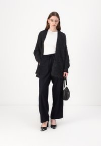 Svart, fuzzy cardigan over en hvit topp, kombinert med marineblå, stripete bukser. En svart håndveske og lakkhælestøvletter fullfører antrekket.