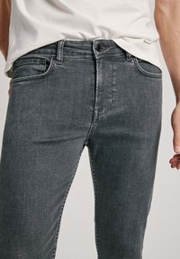 Hallid denim püksid slim fit lõikega, peene tekstuuriga, viie taskuga disain ja õmblusdetailid. Kanda heledat särki.