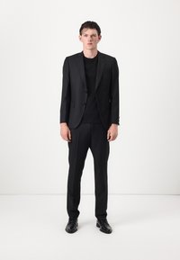 Abito nero a righe sottili su misura con pantaloni abbinati. Tessuto morbido, blazer a due bottoni e calzature nere. Design semplice ed elegante.