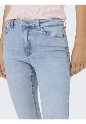 Lyseblå jeans med højtalje, båret med en lyserød strikket top, med frontlommer, en knap og en ring på højre hånd.