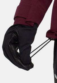 Svart och mörkröd skidvante med texturerad läderhandflata, elastisk mudd och justerbar dragsko för en säker passform.