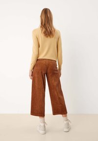 Un pull en tricot beige associé à un pantalon ample en toile marron texturé. Des chaussures légères complètent la tenue, mettant en avant un style décontracté et relaxed.