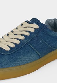 Μπλε τζιν αθλητικό παπούτσι με μπεζ κορδόνια και καφέ λαστιχένια σόλα, δείχνοντας πλευρικές και πάνω λεπτομέρειες σε λευκό φόντο.