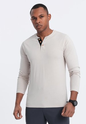 Lys beige langærmet henley skjorte med sort knaplukning og tre knapper. Glat stof med regular fit og rund halsudskæring.