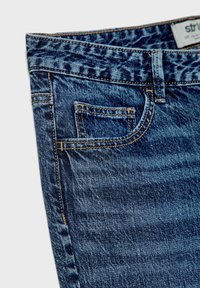 Jean en denim avec une teinte foncée, featuring une poche avant, des coutures contrastantes et une coupe droite. Le matériau semble robuste avec une texture visible.