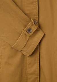 Hellbraune Baumwolljacke mit gefaltetem Kragen und Knopfmanschetten. Die Textur ist glatt mit einem leichten Glanz.