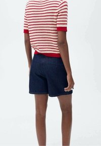 Rood-wit gestreept gebreid shirt met korte mouwen, gecombineerd met donkere denim shorts. Zichtbare stikseldetails en een ontspannen pasvorm.