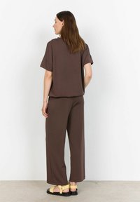 Top marrone e comodo con maniche corte abbinato a pantaloni larghi marroni. Indossato con sandali neri con cinghie giallo chiaro.