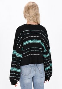 Črn skrajšan pulover s turkizno-belim črtastim vzorcem, dolgimi rokavi in rebrastim ovratnikom, kombiniran z modrimi denim kavbojkami.