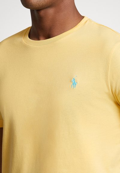 Κίτρινη βαμβακερή μπλούζα με στρογγυλή λαιμόκοψη και κοντά μανίκια. Διαθέτει ανοιχτό μπλε κεντημένο λογότυπο στο αριστερό στήθος. Μαλακή υφή.