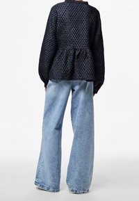 Haut péplum noir texturé avec un col à volants, associé à un jean large bleu clair, présentant un effet délavé et un ourlet effiloché.