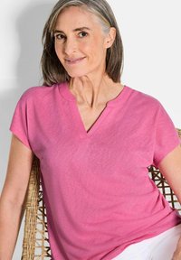 Rosa Baumwoll-T-Shirt mit V-Ausschnitt, kurzen Ärmeln und lockerer Passform. Der Stoff hat eine glatte Textur, und die Farbe ist lebhaft und gleichmäßig.