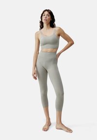 Lichtgrijze naadloze sportset bestaande uit een cropped tanktop met verstelbare banden en high-waisted leggings, beide vervaardigd uit rekbaar materiaal.