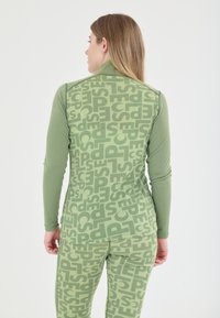 Groene sportoutfit met een langärmige top en leggings. De stof heeft een herhalend groot tekstpatroon in een iets lichtere groene tint.