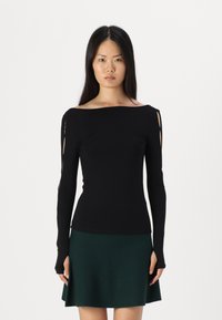 Top negru cu maneci lungi, cu un design off-shoulder și fante tăiate pe brațe. Material neted, formă ajustată, asortat cu o fustă verde.