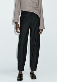 Zwarte op maat gemaakte broek met een losse pasvorm, hoge taille en omslagmanchetten, gecombineerd met een lichtbruine lange mouw top. Soepele stoftextuur.