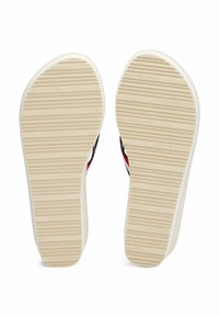 Suola delle scarpe con una superficie beige rigata, caratterizzata da un marchio in rilievo. Accenti neri e rossi visibili lungo i lati. Design piatto ed ergonomico.