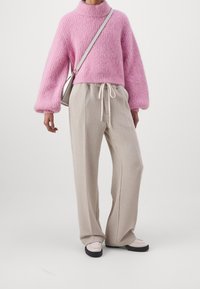 Roze gebreide trui met een hoge kraag, gecombineerd met beige wijde broek met een trekkoord. Gebreide textuur, minimale hardware accenten.
