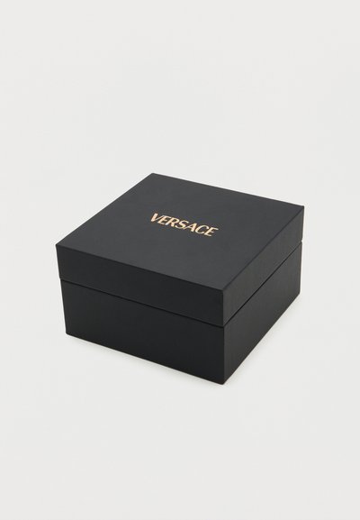 Μαύρο τετράγωνο κουτί με χρυσό λογότυπο VERSACE στο κέντρο του καπακιού, τοποθετημένο σε απλό λευκό φόντο.