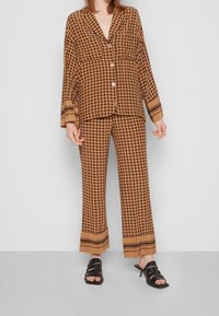 Brun mönstrad co-ord set med en knäppjacka med trumpetärmar och matchande byxor med en kontrasterande rand i fållen. Svarta knäppa sandaler.