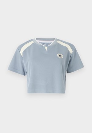 Világoskék anyagú, rövid ujjú cropped póló. Krém színű díszítésekkel és kör alakú logóval a mellkason. Kerek nyakkivágású.