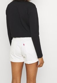 Felpa nera corta con maniche lunghe, abbinata a pantaloni in denim bianchi con orli arrotolati e un'etichetta rossa sulla tasca posteriore.