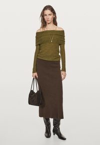 Olijfgroene off-the-shoulder ribbed trui, bruine midi-rok, kniehoge bruine leren laarzen en een zwarte handtas. Eenvoudige gouden ketting als accent.