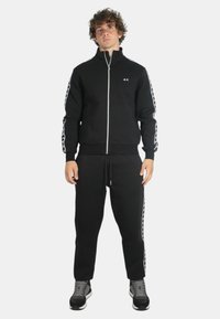 Felpa nera con zip e colletto alto, abbinata a pantaloni jogging neri coordinati; entrambi presentano una texture morbida.