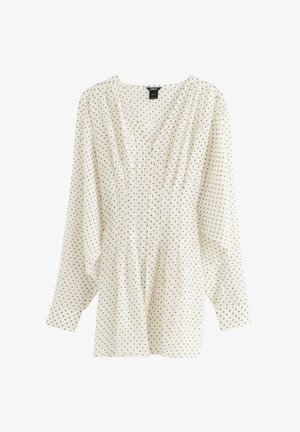 Camicia bianca con maniche lunghe, scollo a V, dettagli con pieghe sottili e pois marroni uniformemente distribuiti. Tessuto leggero con una silhouette fluente.