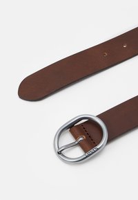 Ceinture en cuir marron avec une texture lisse, dotée d'une boucle ovale en métal argenté. Le cuir présente plusieurs trous de réglage près de la boucle.