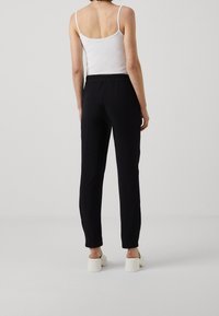 Černé tapered kalhoty s elastickým páskem, kombinované s bílým tílkem. Hladká tkanina a jednoduchý design, žádné viditelné vzory nebo kování.
