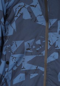 Blauwe jok met een abstract geometrisch ontwerp, textiel stof, een rits aan de voorkant en een knoopdetail nabij de zoom.