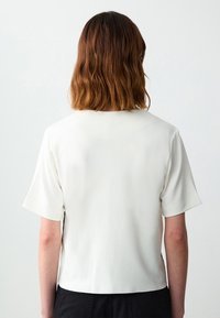 Weißes Kurzarmhemd mit rundem Ausschnitt und glatter Textur, featuring einem geraden Schnitt und minimalen Designdetails.