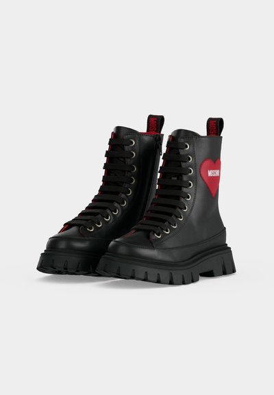 Bottes épaisses noires à lacets avec semelles épaisses, fermeture éclair sur le côté, languettes rouges et détail de cœur rouge avec texte blanc sur les côtés extérieurs.