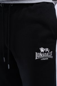 Black joggers made of cotton with an elastic waistband, featuring a white embroidered logo and lion design on the left thigh.