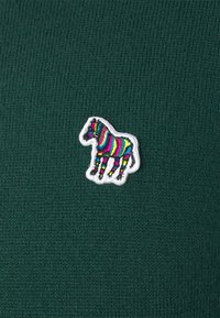 Tessuto a maglia a coste verde scuro con una colorata toppa ricamata a forma di zebra, con strisce rosa, gialle e blu contornate di bianco.
