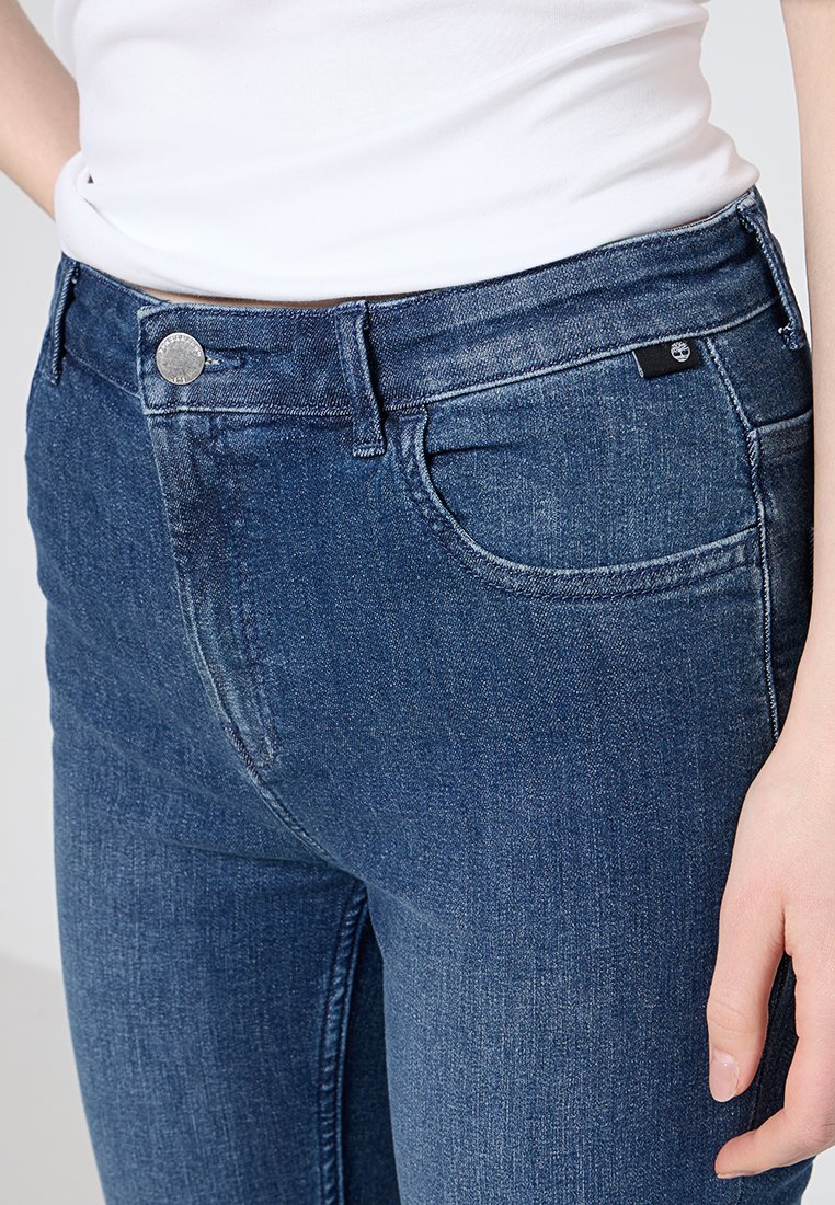 Ciemnoniebieskie dżinsy o wysokim stanie, z pięcioma kieszeniami i srebrnym zapięciem. Miękka tekstura z delikatnymi akcentami przecierania.