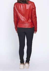 Rød lædermotorcykeljakke med ribstrikkede detaljer på skuldre og ryg, kombineret med sorte slim-fit bukser og hvide sneakers.