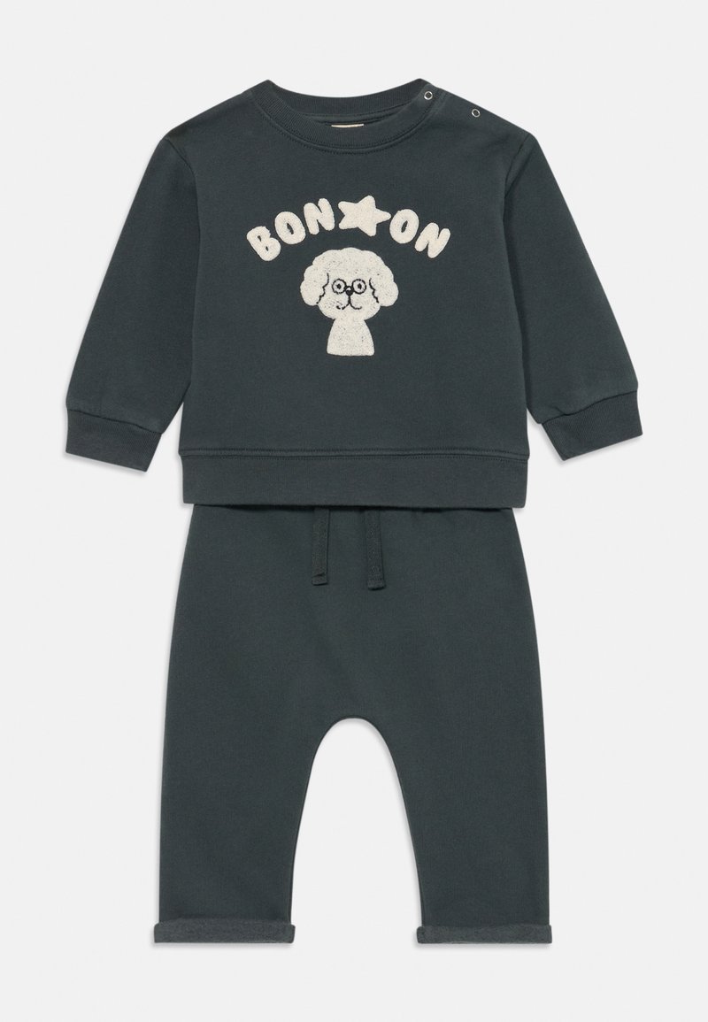 Conjunto de niño pequeño en verde oscuro, con sudadera de manga larga que presenta un perro de dibujos animados con gafas y el texto "BON ON", combinado con pantalones a juego.