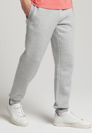 Pantaloni della tuta grigi realizzati in materiale morbido, caratterizzati da un design affusolato, tasche laterali e polsini a costine alla caviglia. Abbinati a scarpe da ginnastica bianche.