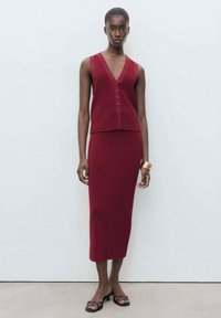 Top senza maniche in maglia color bordeaux con scollo a V e dettagli di bottoni, abbinato a una gonna fitted di lunghezza ginocchio in tessuto texturizzato, design minimalista.