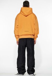 Orange oversized hoodie with a large hood and ribbed cuffs, paired with black cargo pants featuring multiple pockets and a relaxed fit.