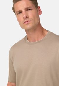 Beige krūšdaļa T-krekls, izgatavots no gludas, vieglas auduma. Iespējas ar īsām piedurknēm un smalku, vienmērīgu tekstūru.