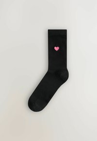 Schwarze Socken aus einem glatten Stoff, mit einem kleinen roten Herz, das nahe dem Knöchel gestickt ist. Einfaches Design mit verstärkter Zehenpartie.