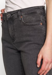 Faded svarta jeans i denim med medelhög midja, femfickorsdesign, kopparnitar och en slät textur, visade från midjan och ner.